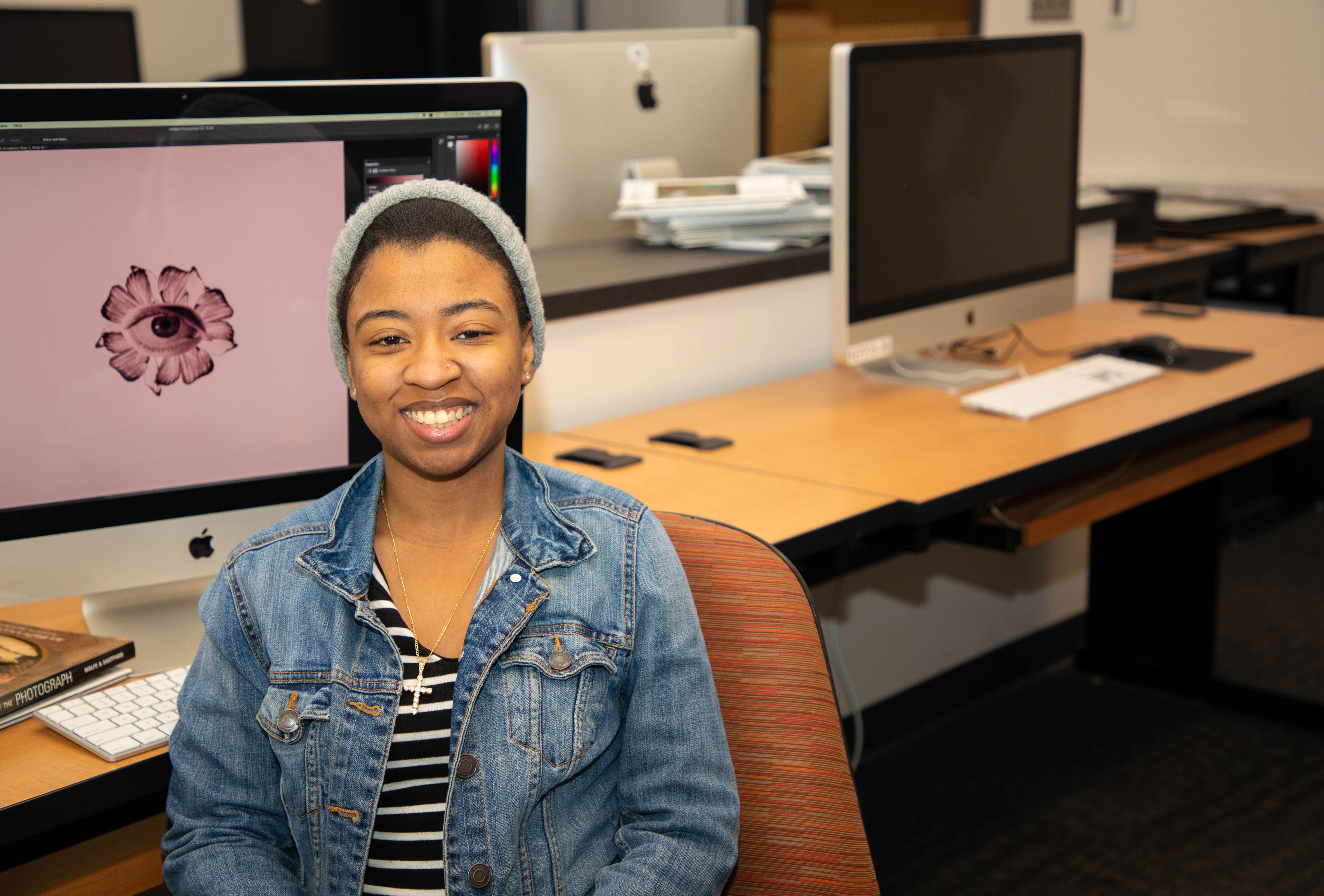 Student posing in MAC lab in front of design work