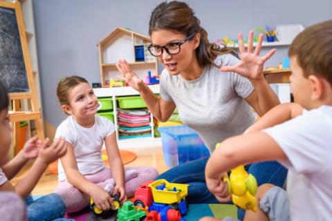 Female teacher playing with children on the floor of child care room.