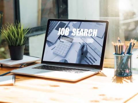 A laptop sitting in the sunlight on a desk with a search bar on the screen that says "Job Search"