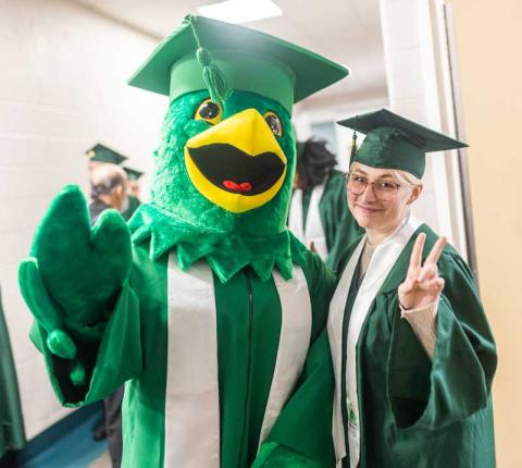 Hawkeye, HCC's mascot, standing next to an HCC graduate