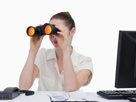 A job seeker sitting at a desktop computer while looking through binoculars